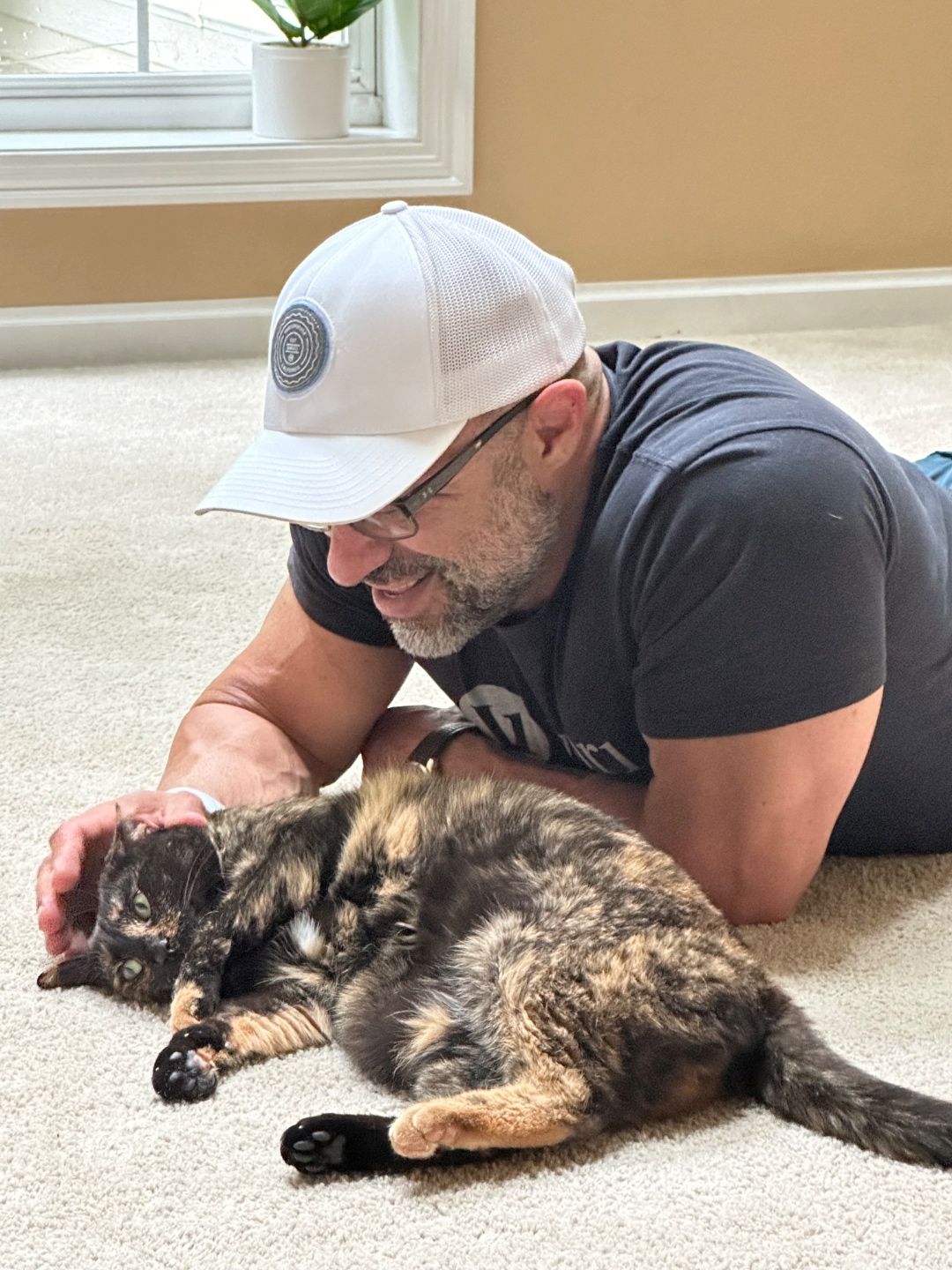 Anthony Castore lying on the floor petting Hannah, his tortoiseshell rescue cat.