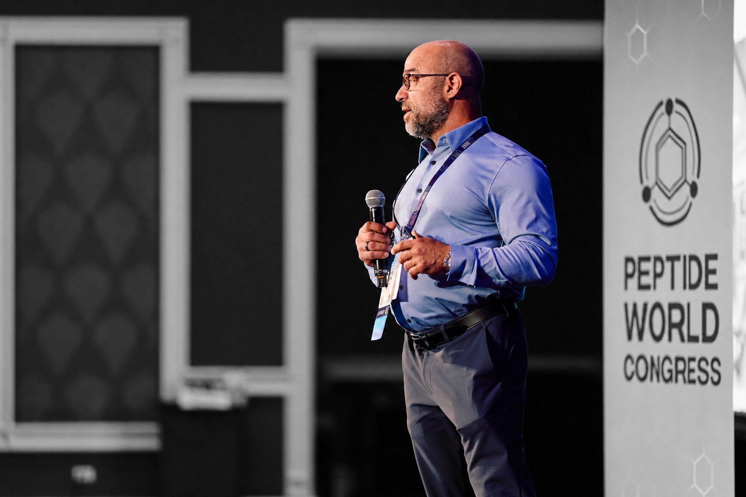 Anthony Castore on the main stage at the SSRP Peptide World Congress, speaking with a microphone.